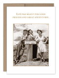 Three women pose joyfully by a sign reading Glacier Vista Elev. 6000, with majestic mountains in the background, evoking a sense of nostalgia similar to vintage photos. The image is beautifully framed with the text: "Life was meant for good friends and great adventures," from the Great Adventure Birthday Card by Shannon Martin Design.