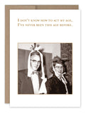 The "Act My Age Birthday Card" from Shannon Martin Design features a vintage photo of a man and woman in playful hats. The card's message humorously states, "I don't know how to act my age, I've never been this age before." It comes with an eco-friendly Kraft envelope made from recycled paper. Happy Birthday!