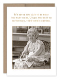 A black-and-white image of an elderly woman sitting in a chair, wearing glasses and a shawl, holding a piece of recycled paper. The text above reads, "It's never too late to be what you want to be. Unless you want to be younger, then you're screwed." This delightful scene is brought to you by the Never Too Late Birthday Card from Shannon Martin Design.