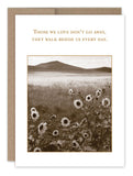The Walk Beside Us Sympathy Card by Shannon Martin Design showcases a sepia-toned image, reminiscent of vintage photographs, depicting a field of sunflowers with rolling hills in the distance. The text above the scene reads: "Those we love don‚Äôt go away, they walk beside us every day." Expertly crafted on recycled paper, this card is elegantly paired with a brown envelope.