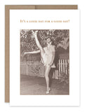 A vintage photograph showcasing a smiling woman in a short dress and shoes, executing a high kick outdoors beside a picket fence and trees. Presented on recycled paper by Shannon Martin Design, the card is titled "It's A Good Day Birthday Card" and reads, "It's a good day for a good day!
