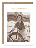 A woman dressed in vintage clothing and a sailor hat beams with joy as she holds a ship's wheel. This sepia-toned image is printed on FSC-certified recycled paper by Shannon Martin Design, bordered with a simple frame, and features the message "Let joy be your compass" above it. The product is named "Joy Be Compass Birthday Card.