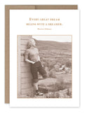 A sepia-toned image of a young woman leaning against a wooden structure, gazing into the distance, wearing a sweater and rolled-up jeans with a rural landscape in the background. Printed on recycled paper, the card from Shannon Martin Design features the quote: Every great dream begins with a dreamer. This is the Every Great Dream Encouragement Card.