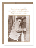 A vintage sepia-toned photograph on the "Shuts Door What A Hoot Card" by Shannon Martin Design captures a person smiling as they open a door. The text above reads, "When life shuts a door, just open it again. It's a door. That's how they work." This snapshot echoes the charm of timeless vintage photos, infusing hope and simplicity into everyday moments.