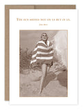 A vintage-style photo on recycled paper showcases a person wrapped in a striped towel, smiling on a sandy beach with dune grass. The Sun Shines Birthday Card from Shannon Martin Design includes the quote: "The sun shines not on us but in us." - John Muir.