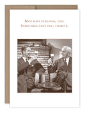 A sepia-toned photograph of two men in suits, sitting on armchairs with smiles, raising their glasses of beer in a toast. The caption above them says, "Men Have Feelings Birthday Card." Designed by Shannon Martin Design, this card captures the timeless camaraderie of the duo against a warm fireplace backdrop, reminding us that sometimes men's feelings are simply thirsty.