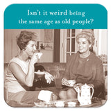 Two women dressed in vintage clothing sit on a couch enjoying tea, their cups placed elegantly on Shannon Martin Design's chic Same Age Coasters. A teapot adds to the perfect hostess gift scene, while the image humorously asks, "Isn‚Äôt it weird being the same age as old people?